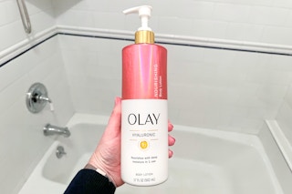 someone holding a bottle of olay lotion in a bathroom