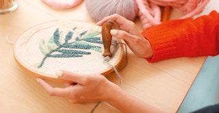 A person using a punch needle to make a pattern of a leaf on an embroidery hoop