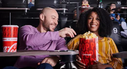 a couple at a movie theater with popcorn and a drink