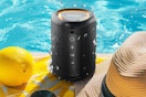 The lighted color changing waterproof bluetooth portable speaker sits on the edge of a swimming pool between a citrus fruit & hat.