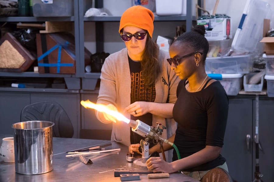 Two people standing in a crafting studio, using a torch in their process.