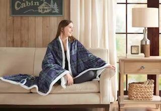 woman sitting on a couch with a woolrich heated blanket around her