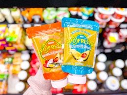 hand holding two avofresco guac pouches in walmart aisle