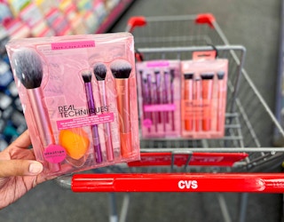hand holding one Real Techniques makeup brush sets in front of cart with two other sets