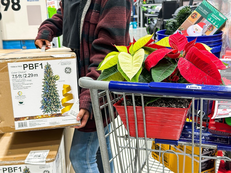 a person lifting a fake christmas tree to place into a lowes cart