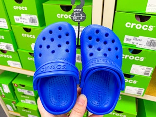 Woman holding up a pair of blue kids crocs at the shoe store