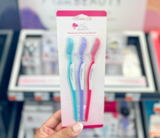 hand holding pack of Plum Beauty eyebrow shaping razors in front of display
