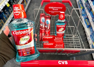 A person's hand holding a bottle of Colgate Total mouthwash above a CVS shopping cart with more Colgate mouthwash, Colgate Optic White ...