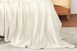 Lifestyle image of the beige Kayamas blanket draped over bed (close up shot)