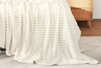 Lifestyle image of the beige Kayamas blanket draped over bed (close up shot)