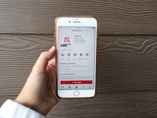 hand holding phone in front of house with coupon on phone screen