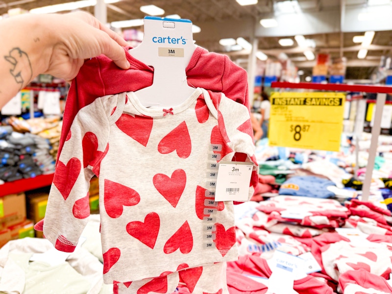 person holding a carter's baby outfit set by a sign for $8.87