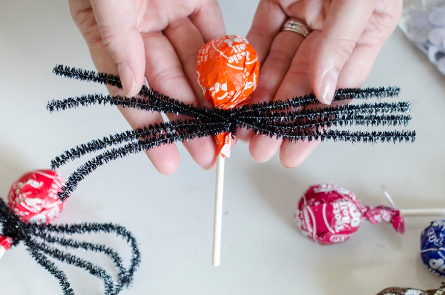 Pipe cleaners being twisted around a lollipop candy.