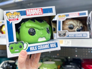 A Funko Pop mug held out by hand in front a store shelf with other Funko Pop mugs sitting on a store shelf.