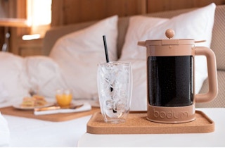 stock photo of bodum bean cold press and coffee maker on tray with glass on top of bed
