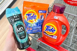 person placing downy unstoppables into a cart with tide pods and laundry detergent in it