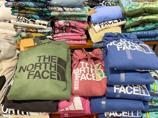 A variety of The North Face hoodies folded on a shelf at Dicks Sporting Goods