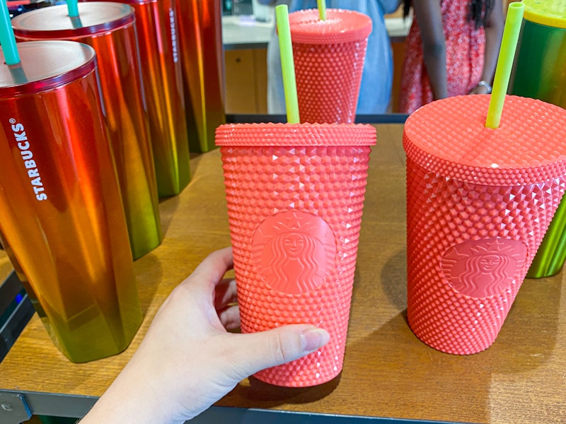 woman holding pink reusable Starbucks tumbler on shelf