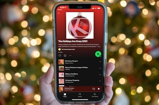 A person holding up a cell phone with a Christmas tree in the background displaying a Spotify Christmas playlist