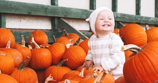 smiling toddler surrounded by pumpkins