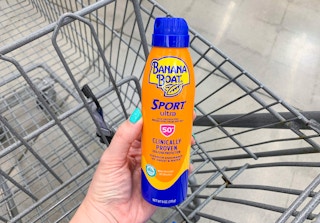 orange and blue bottle of banana boat sport ultra sunscreen spray held by woman's hand over walmart cart