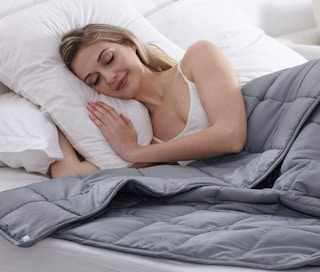 a woman with a grey weighted blanket on a bed