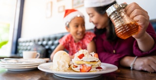 mother and child during christmas pouring syrup on pancakes at restaurant