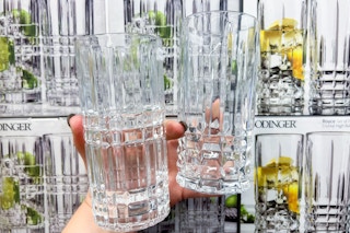 Hand holding two high ball crystal glass in front of boxes of crystal glasses