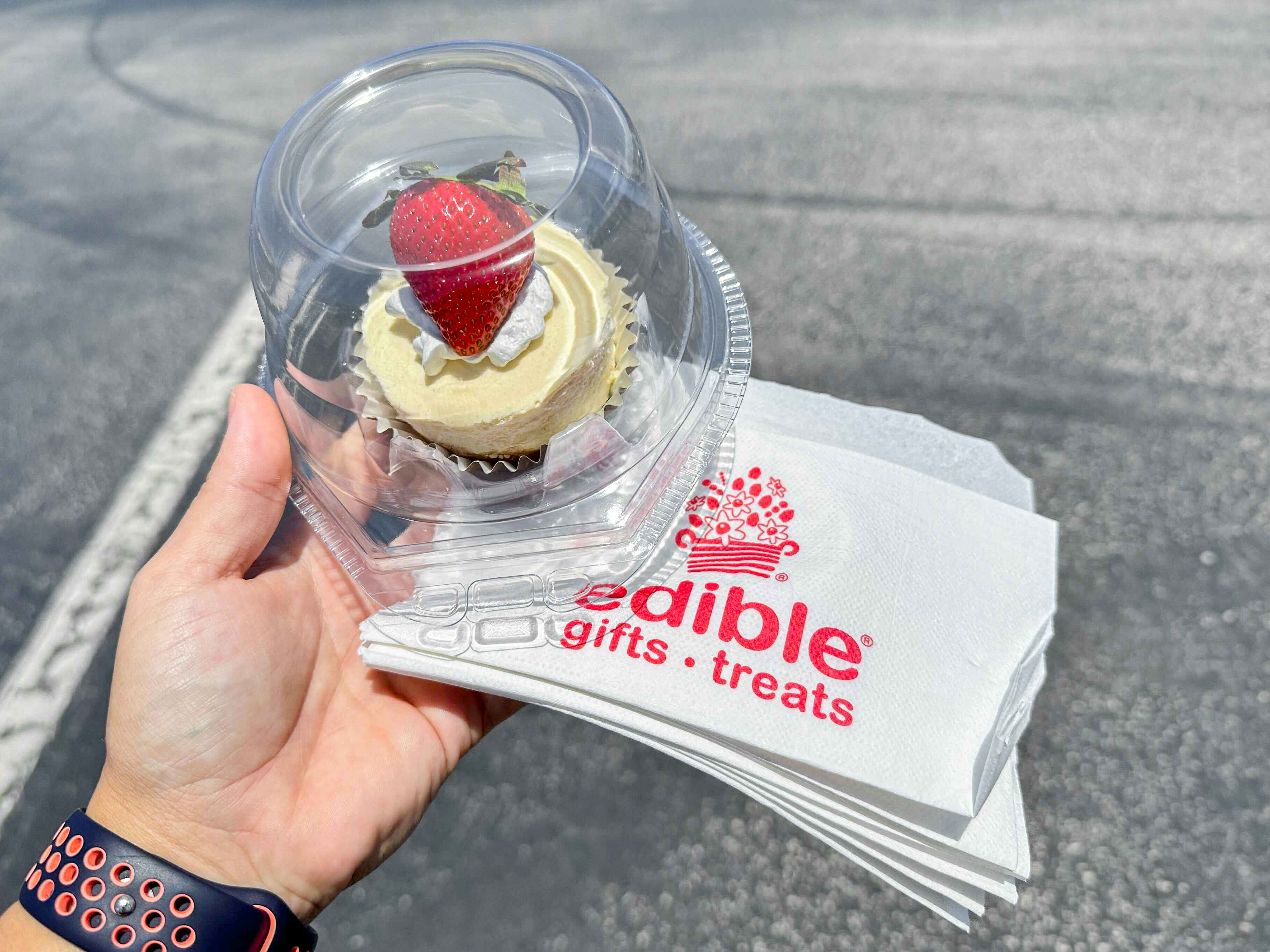 a person holding a cupcake with a strawberry on top