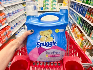 A jug of snuggle super fresh fabric softener held out in front of cart and store aisle.