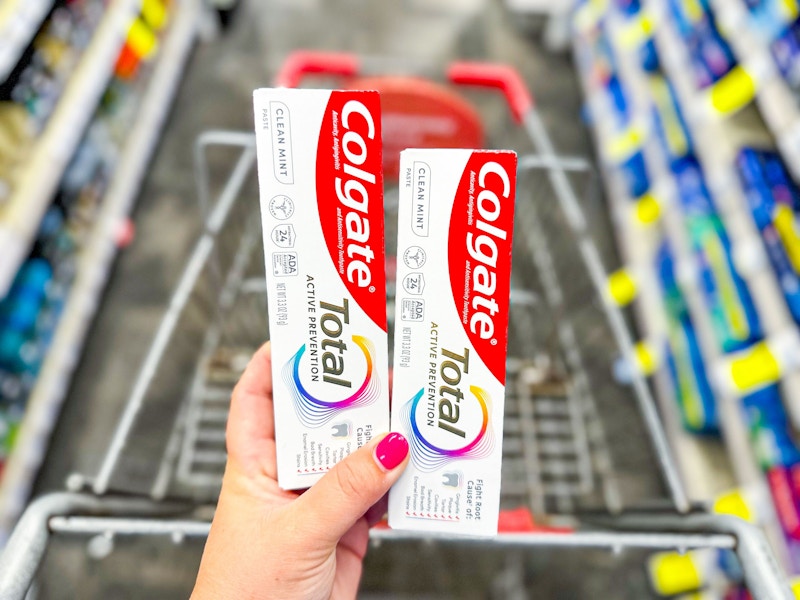 person holding 2 colgate total toothpastes over a cart