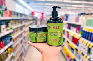 person holding a bottle of mielle shampoo and a jar of mielle hair mask in an aisle
