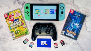 A Nintendo Switch, pro controller, and Best Buy gift card next to some switch video games.