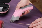 person cutting purple fabric with electric scissors