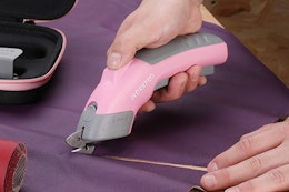 person cutting purple fabric with electric scissors