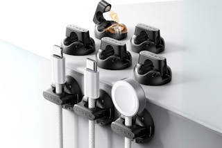 A set of eight cable clips with magnetic open and close mechanisms. Three are adhered to the side of a desk and five are on top.
