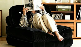 a person sitting on a foldable sofa chair reading