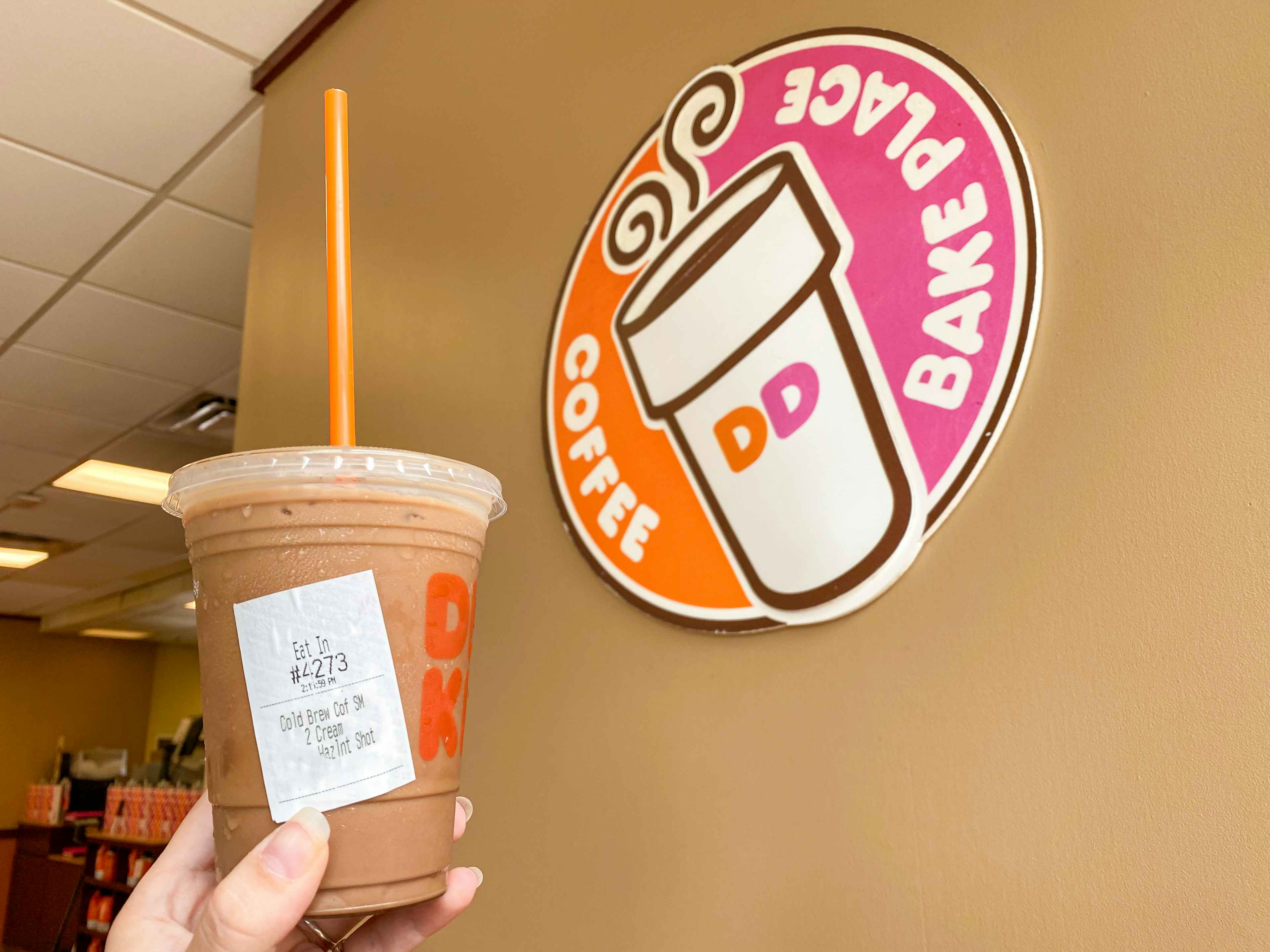 person's hand holding a dunkin' cold brew near store signage