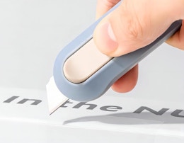 a hand using a blue box cutter on paper