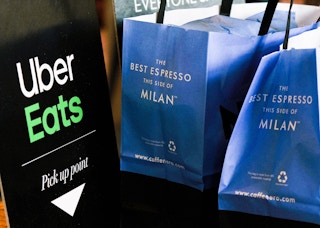An Uber Eats sign next to two bags from Caffe Nero in Milan next to it