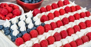 Patriotic, red white and blue, American flag cake. Fresh blueberries and raspberries in the background
