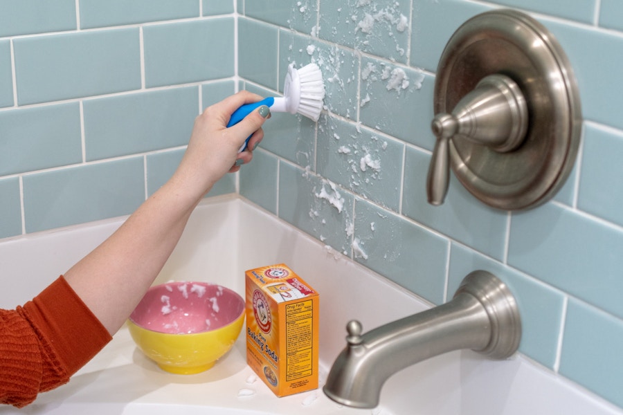 A person scrubbing bathtub tile with baking soda.