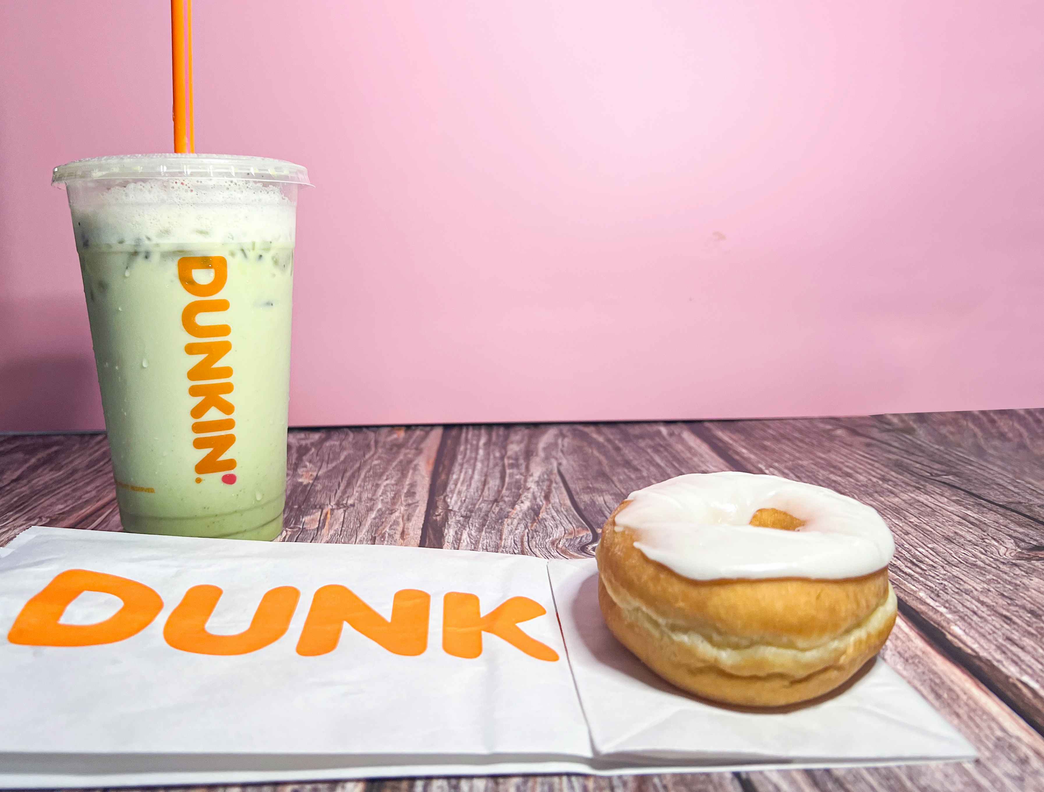 White glazed donut from dunkin donuts along with a green matcha drink against a pink background