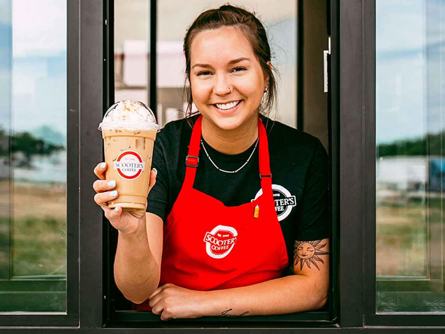 a person holding up a coffee from scooters coffee while smiling