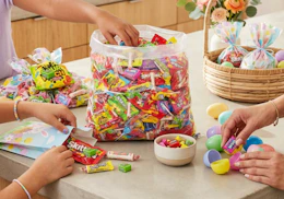 a bulk bag of candy on a table with people filling Easter eggs