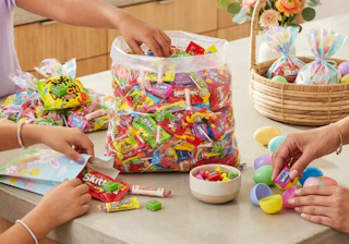 a bulk bag of candy on a table with people filling Easter eggs
