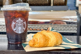 a tall starbucks iced coffee and croissant sitting on a counter 