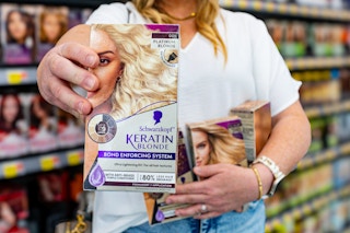 a woman holding schwarzkopf keratin blonde hair dye in walmart