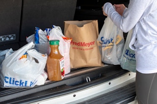 A person setting some Fred Meyer grocery pickup groceries in the trunk of a vehicle.