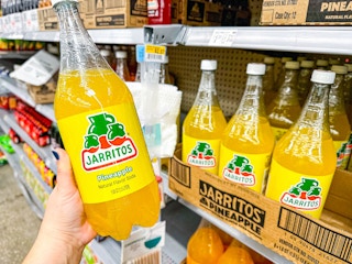 A pineapple Jarritos soda held up in soda aisle of Walmart